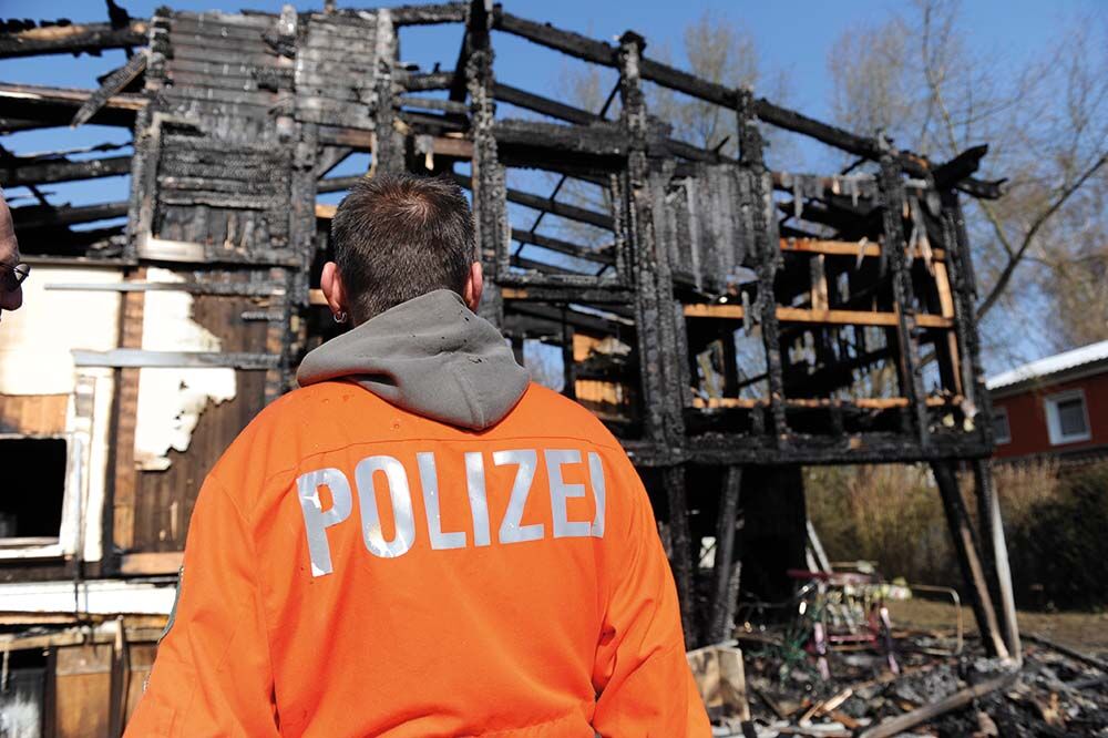 Mann mit Weste mit der Aufschrift Polizei bei einer Brandermittlung